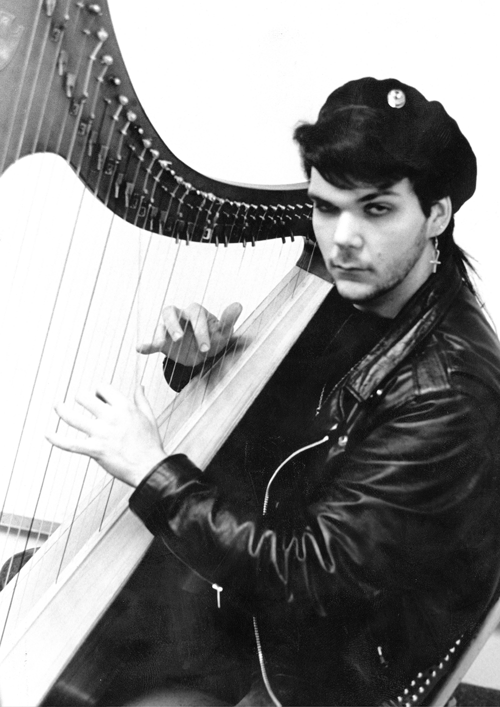 black and white image of early twenties man in a black beret and leather jacket playing a harp