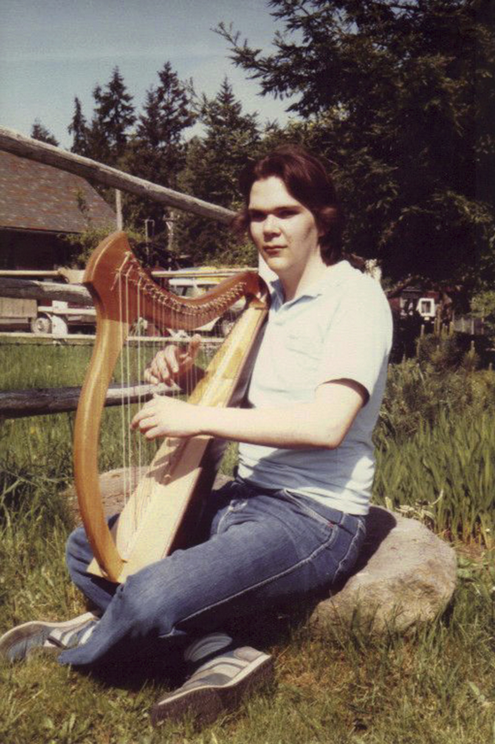 teenage boy seated on rock with small harp