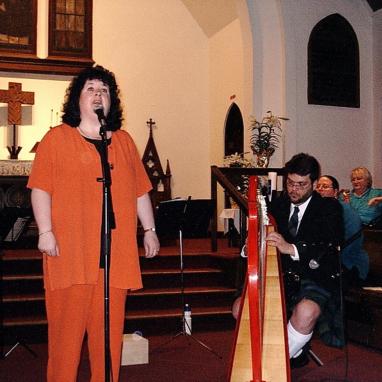 woman singing into microphone accompanied by man at harp