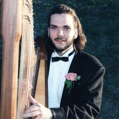 man seated behind small pedal harp