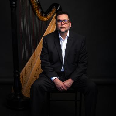 man seated in front of classical harp