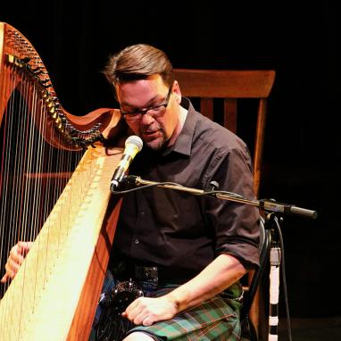 man in kilt behind harp