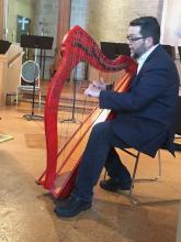 man seated at small red harp singing